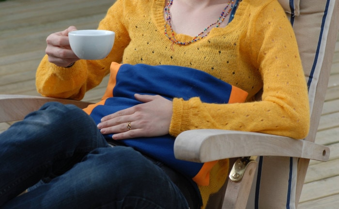 Frau mit Bauchschmerzen und Tee in der Hand: Der PH-Wert des Stuhls ist die erste wichtige Information, die ein Stuhltest zur Verfügung stellt.