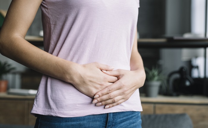 Frau mit Händen auf ihrem Bauch: Ein Stuhltest kann dabei helfen, herauszufinden, wo Bauchschmerzen herkommen.