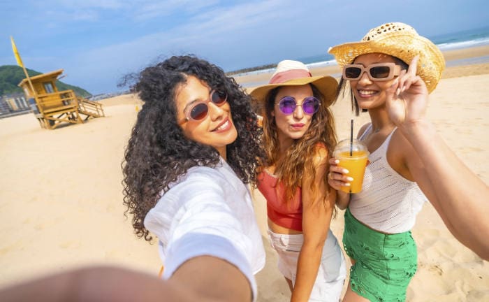 Junge Frauen schießen Fotos am Strand: Junge Versicherungskunden schließen mehr Versicherungen ab als ältere.