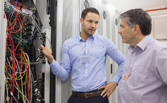 Mitarbeiter und Chef diskutieren in einem Serverraum: Vor dem Abschluss einer Cyberversicherung sollten Unternehmer ihre IT auf den aktuellsten Sicherheitsstand bringen.