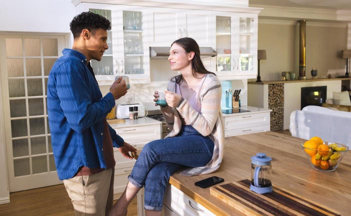Junges Paar sitzt in der Küche ihres Hauses und trinkt einen Kaffee: Ein Immobilienkauf ist für die meisten die größte finanzielle Transaktion ihres Lebens