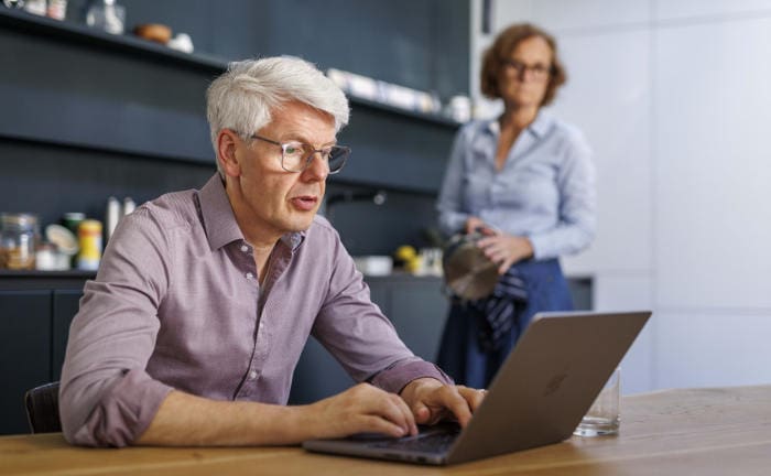 Rentner sitzt in der Küche und surft auf seinem Laptop: Mit einer Fondsrente können Rentner ihre Altersvorsorge ausbauen.