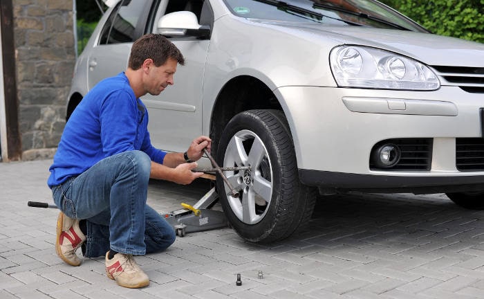 Mann wechselt Reifen an seinem Auto: Winterreifen erhöhen die Sicherheit bei Eis und Schnee.