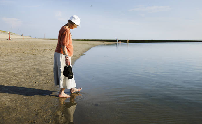 Rentnerin spaziert mit nackten Füßen am Meer: Mit dem richtigen Anbieter und Tarif für die Basisrente können Rentner ihren Ruhestand mehr genießen.