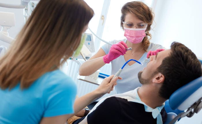 Eine Zahnärztin behandelt zusammen mit ihrer Assistentin einen Patienten: Zahnzusatzversicherungen schließen Kunden ab, um die hohen Kosten für Zahnbehandlungen zu senken.