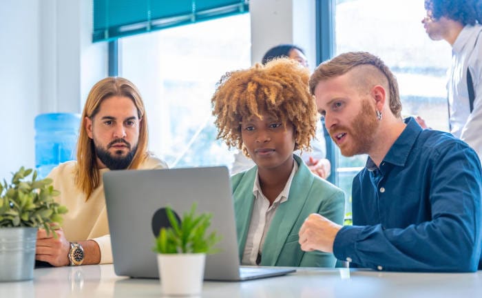 Junge Mitarbeiter besprechen etwas am Laptop: Viele Firmen nutzen ihre bAV, um Mitarbeiter zu gewinnen und zu binden.