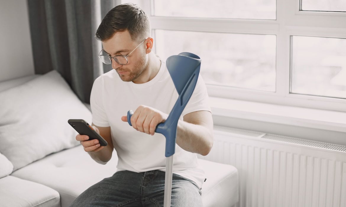 Mann mit gebrochenem Bein schaut auf sein Smartphone: Makler haben in einer aktuellen Umfrage ihre Makler-Champions in sieben Kategorien wie Kranken und Leben bestimmt.