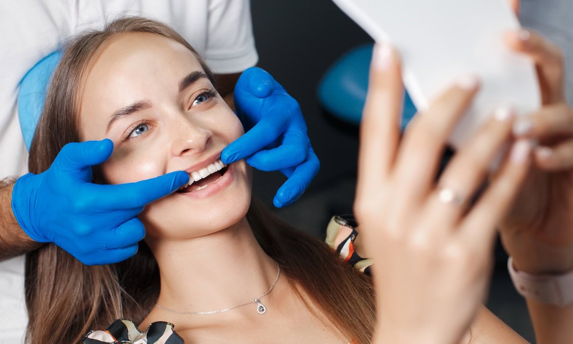 Frau betrachtet ihre behandelten Zähne: Die Analysten von Morgen & Morgen haben sich den Markt für Zahnzusatztarife genauer angeschaut.