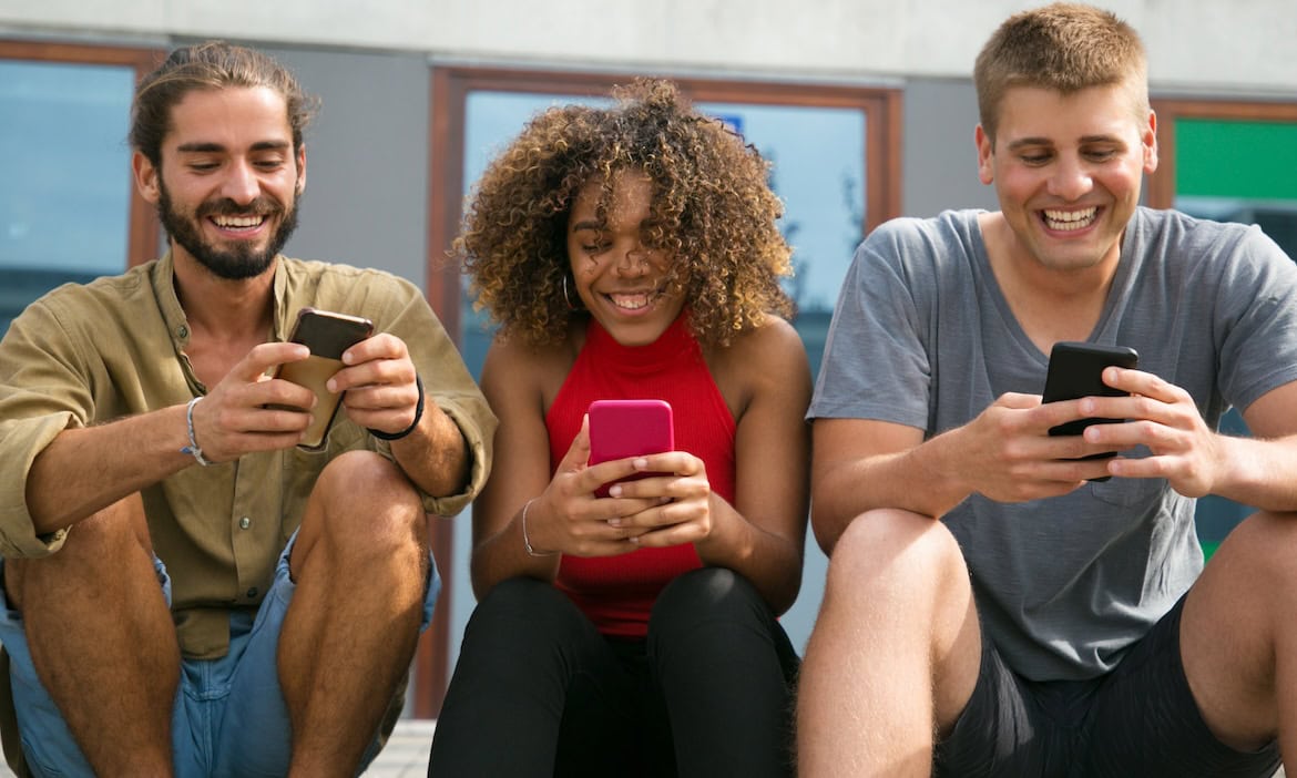 3 junge Personen schauen auf ihre Smartphones: Junge Kunden sind begehrte Kunden für Versicherungsmakler.