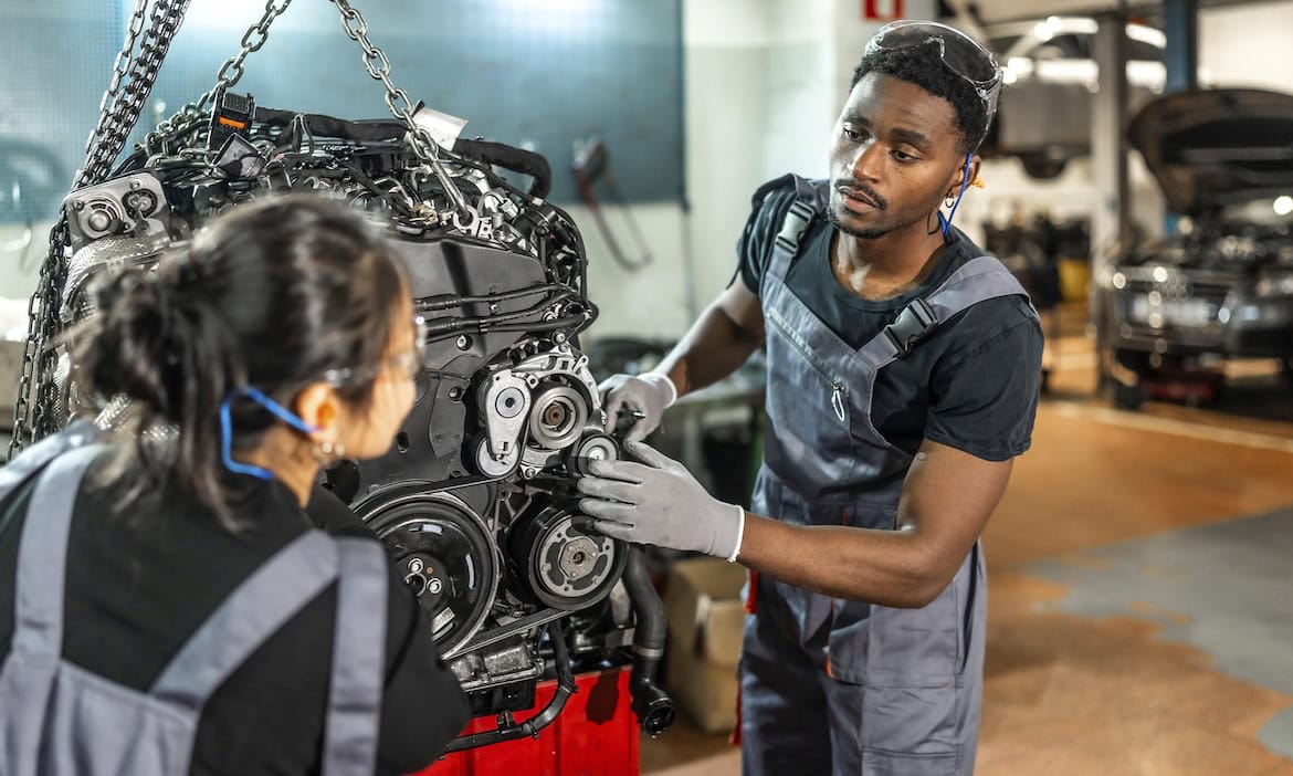 Zwei Automechaniker schauen sich einen Motor an: Weil die Ersatzteilpreise weiter steigen, werden auch die Reparaturkosten 2025 weiter steigen.