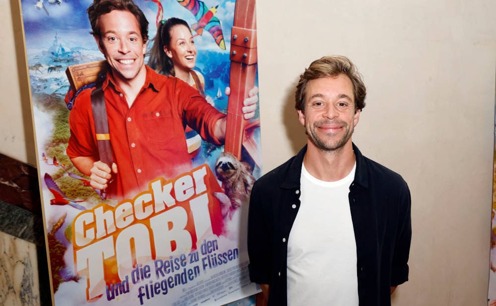 „Checker Tobi“ Tobias Krell im Herbst 2023 mit Plakat für den Film „Checker Tobi und die Reise zu den fliegenden Flüssen“: Zusammenarbeit mit der Allianz