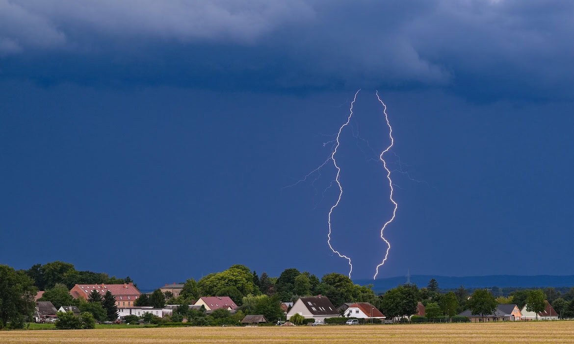 Blitz am Himmel über einem Dorf, Naturgewalt, stürmisches Wetter, dunkle Wolken, ländliche Umgebung.