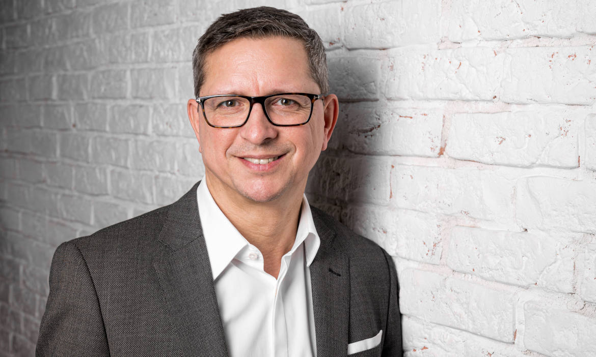 Beraterportrait eines Mannes mit Brille vor weißer Ziegelwand.