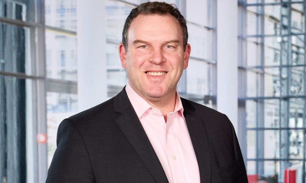 Individu in Geschäftskleidung vor moderner Büroarchitektur, professionell und freundlich.