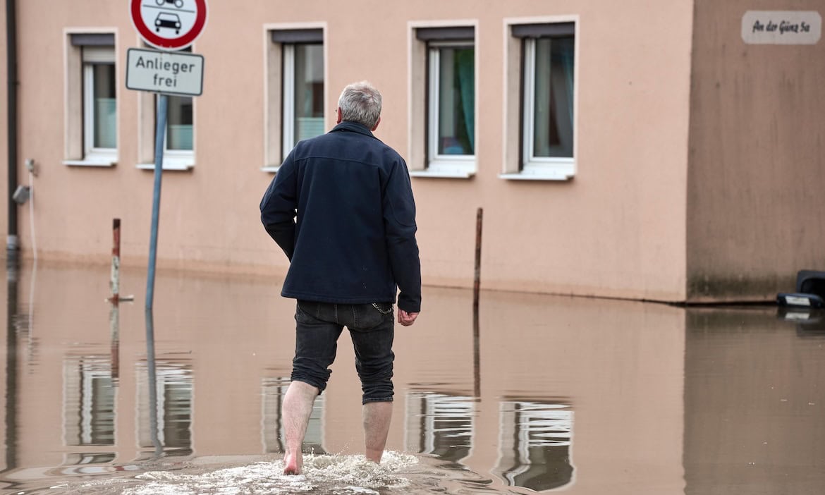 Mann läuft durch überschwemmte Straße nach Extremwetterereignis.