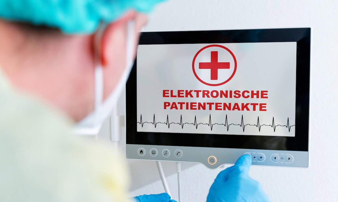 Arzt mit Monitor zeigt elektronische Patientenakte und EKG-Diagramm.