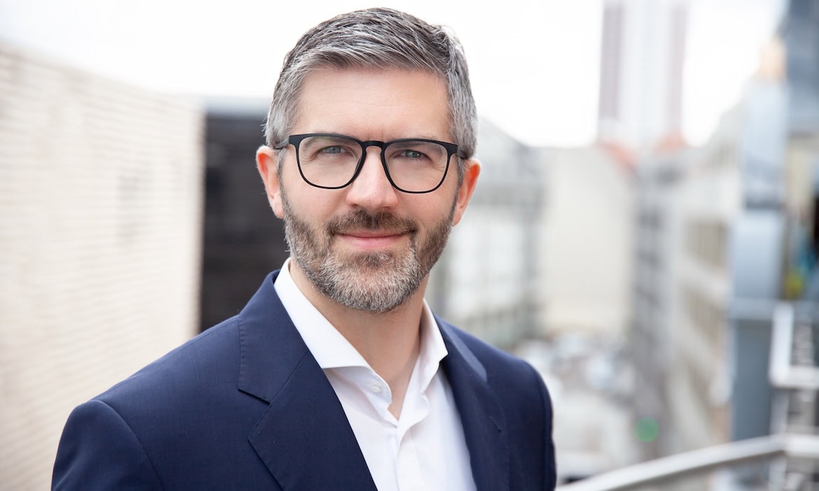 Mann in Anzug auf Dachterrasse mit Stadtblick, Zukunft der Versicherungen.