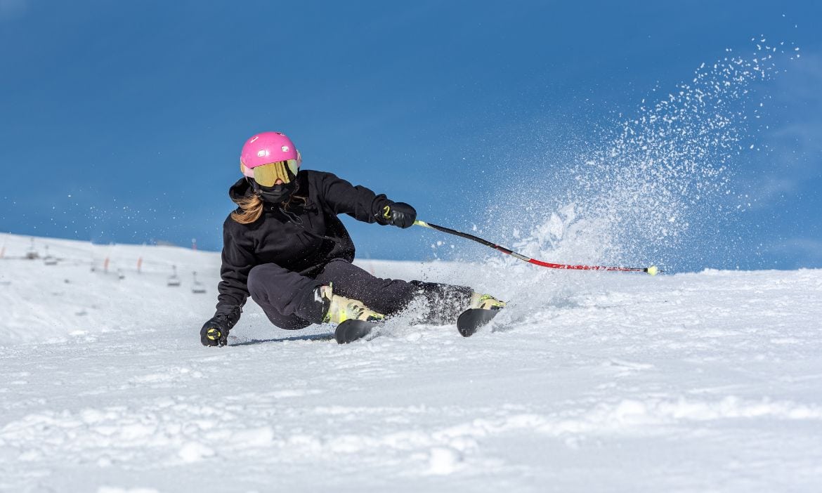 Gleitschirmfliegerin beim Skifahren im Schnee, trägt pinken Helm und schwarze Kleidung.