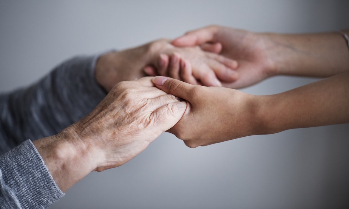 Nahaufnahme von älteren und jüngeren Händen, die sich gegenseitig halten, symbolisiert Pflege und Zu.