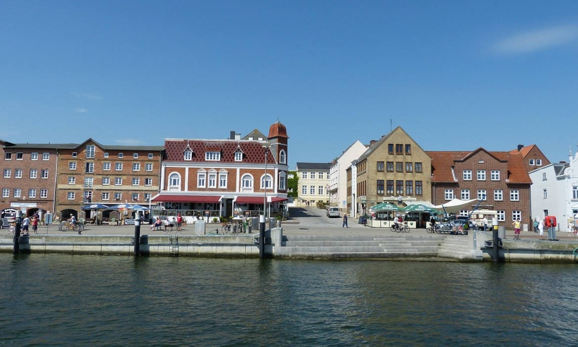 Blick auf den Hafen von Ostangeln mit bunten Gebäuden und Wasser im Vordergrund.