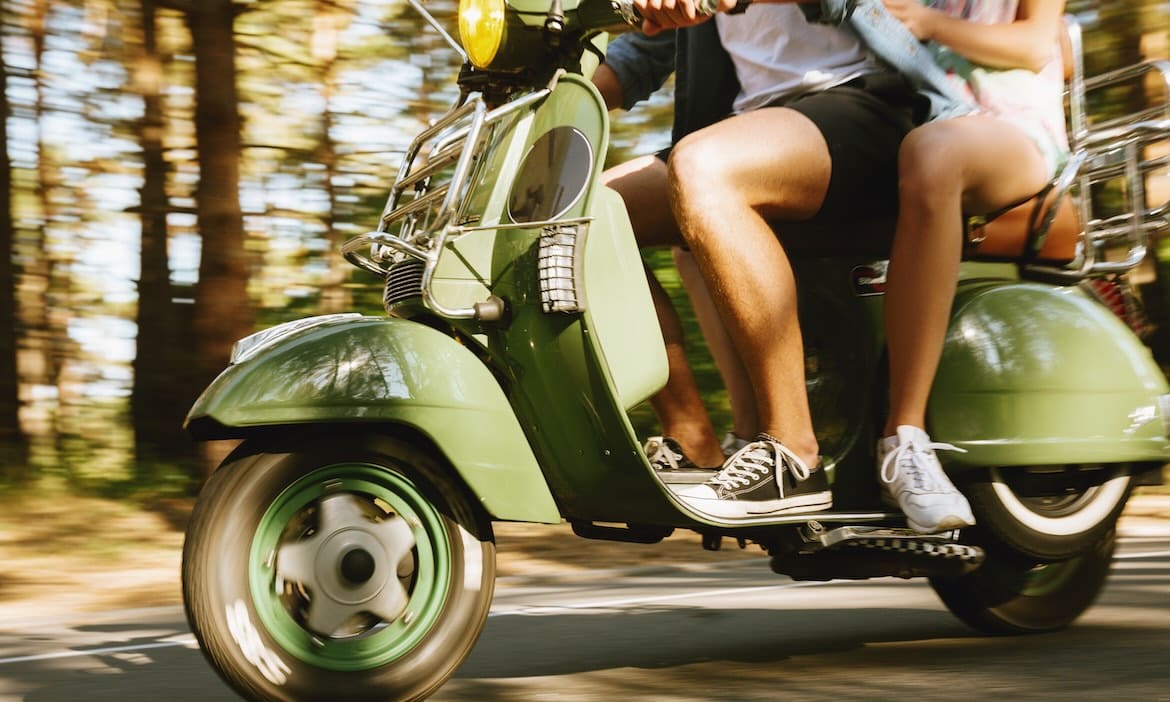 Moped mit Fahrer und Beifahrer auf der Straße, neues Kennzeichen sichtbar.