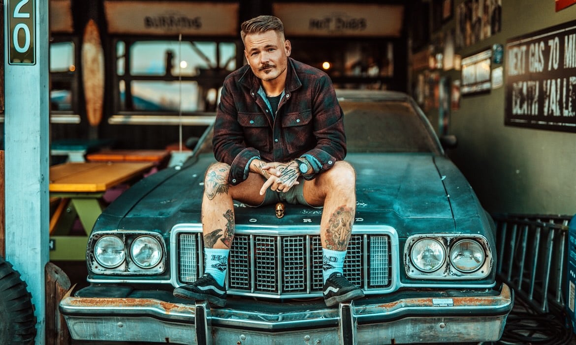 Attraktiver Mann sitzt auf einem alten Auto in einem Café, zeigt Selbstvertrauen und Humor.